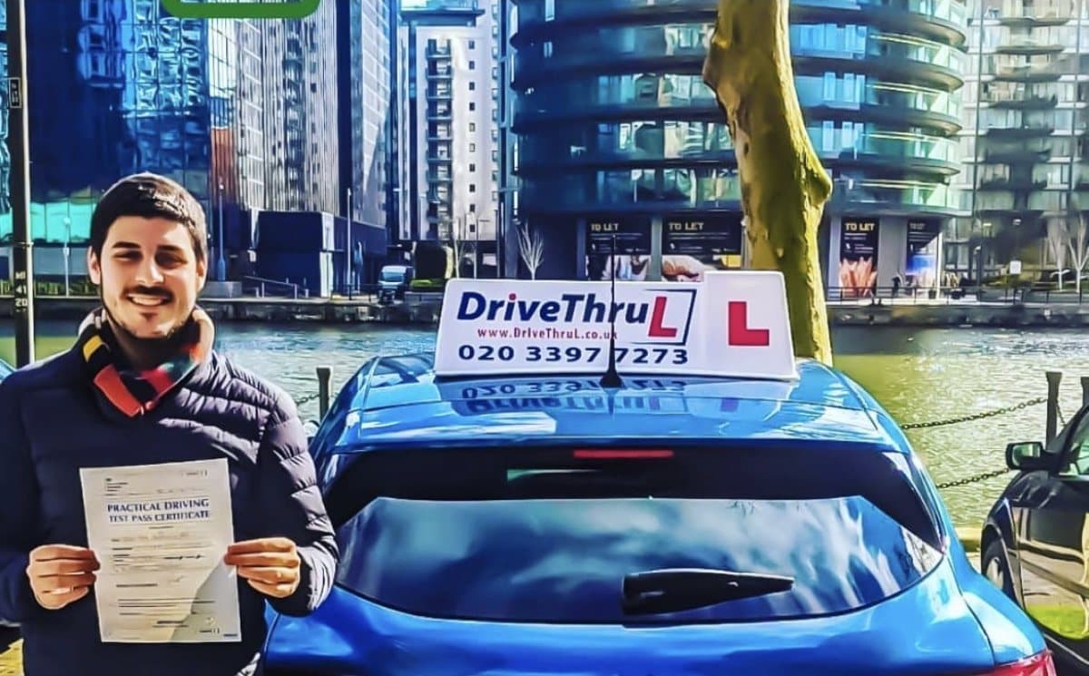 A DriveThruL pupil with his pass certificate beside the driving school car at South Quay, Canary Wharf