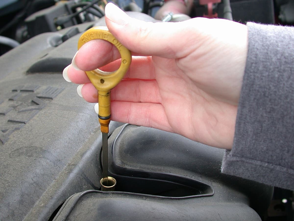 A hand pulling the yellow engine oil dipstick out of an engine
